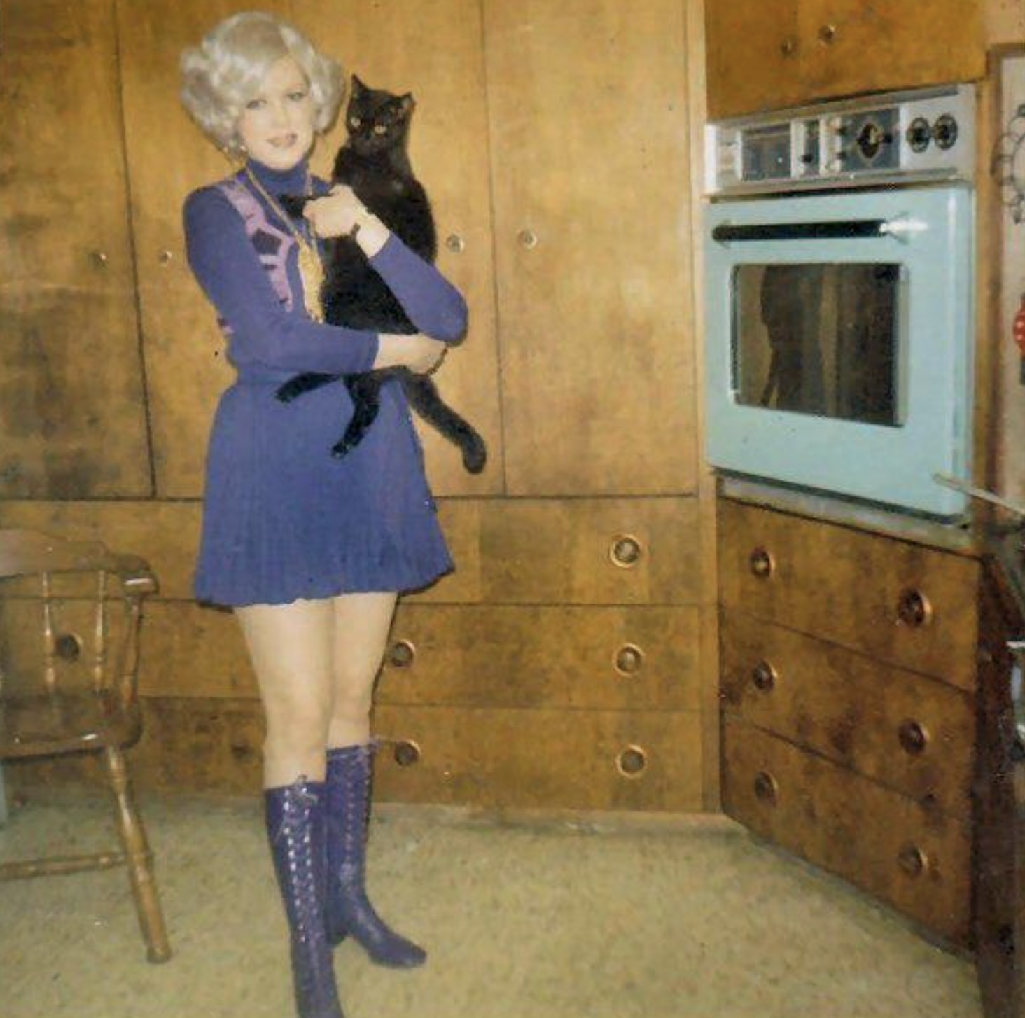 A very stylish wife posing in the kitchen with her cat and turquoise oven. 